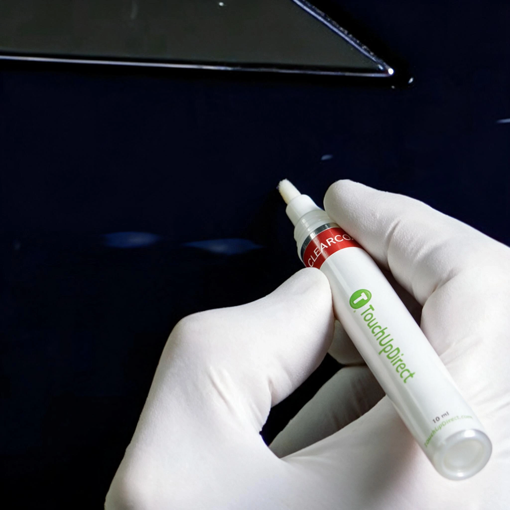 Gloved hand applying colorcoat to a dark vehicle panel without finishing the repair with clearcoat