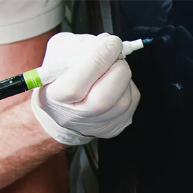 Gloved hand applying blue colorcoat with the pen tip of a combo applicator