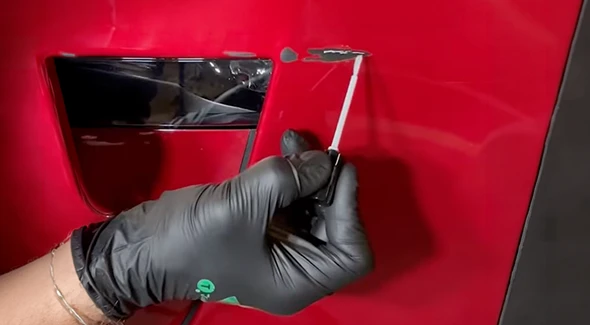Gloved hand applying primer to exposed damage on a red vehicle panel