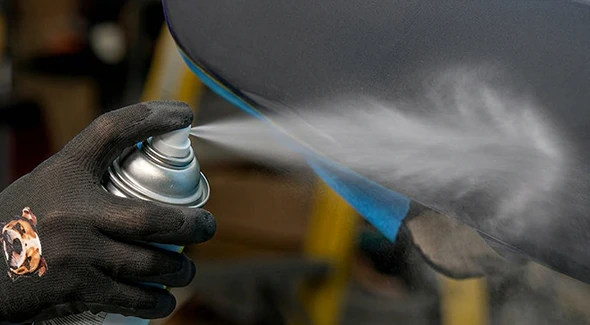 Technician spraying automotive primer onto a vehicle panel with an aerosol can