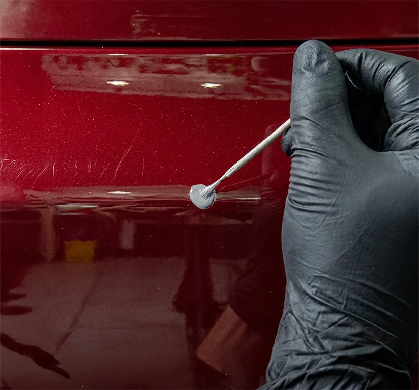 Gloved hand applying too much primer to a scratch on a red vehicle panel