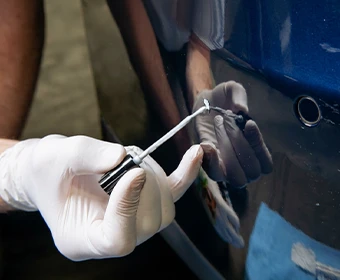 Gloved hand applying primer with a fine brush to a small damaged area on a blue vehicle panel