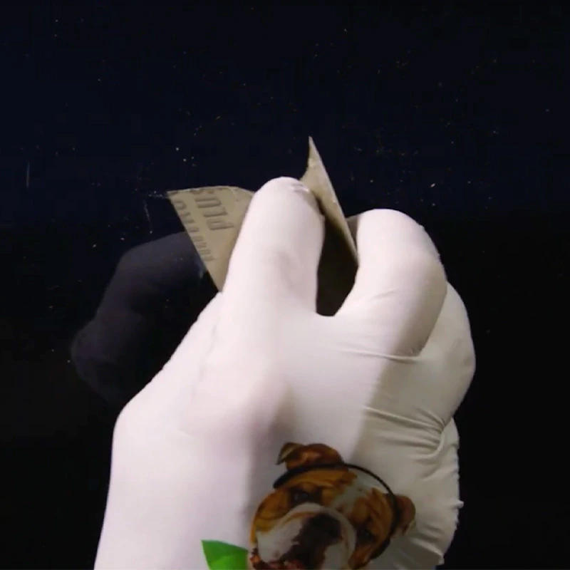 Gloved hand sanding a raised scratch on a dark vehicle panel
