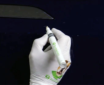 Gloved hand applying primer with a TouchUpDirect pen to a paint chip on a dark blue vehicle panel