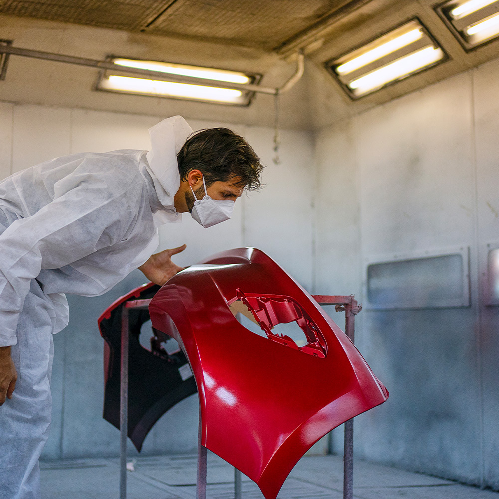 Painter wearing protective equipment while spray painting an automotive panel