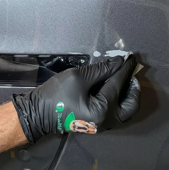 Black-gloved hand sanding a gray primed vehicle panel with a sanding block