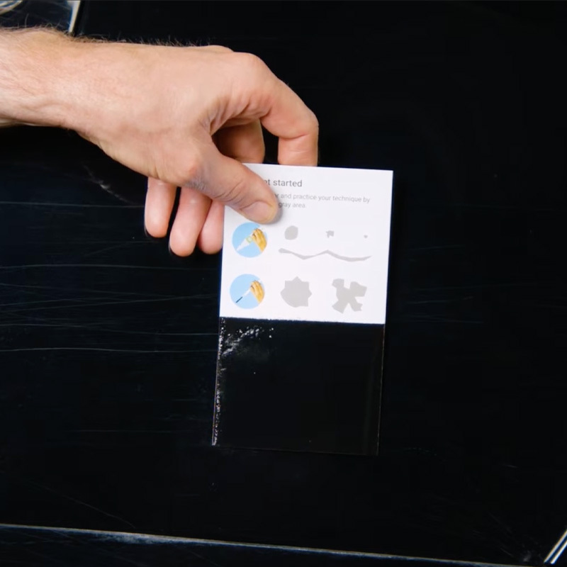 Hand holding a painted test card against a dark vehicle panel to verify the color match.