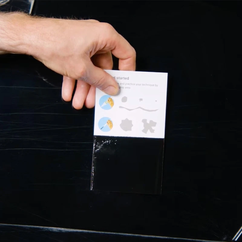 Hand holding a painted test card against a dark vehicle panel to verify the color match.