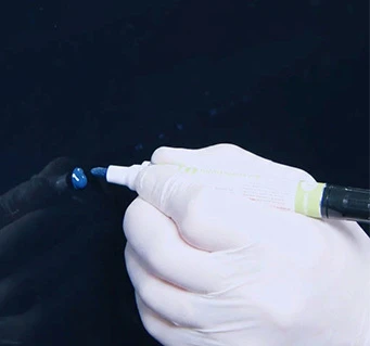 Gloved hand applying too much paint to a vehicle chip with a touch up pen