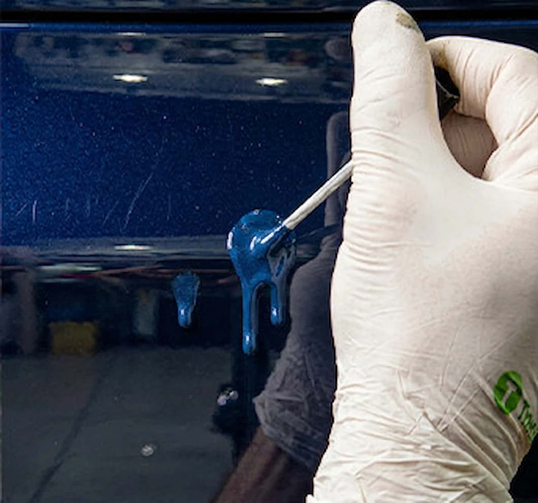 Gloved hand applying a thick coat of blue touch up paint.