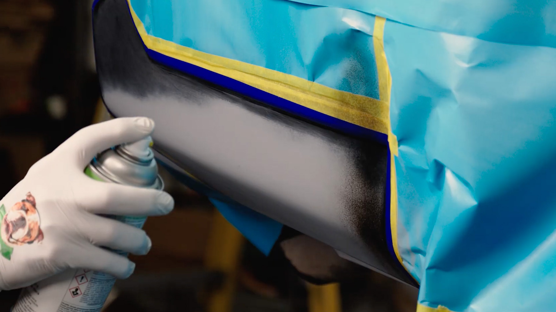 Gloved hand spraying automotive paint onto a masked vehicle panel during a large scratch repair.