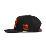 Stilly Boys Clinch hat in black, left side view with blaze orange embroidered interlocking SB monogram