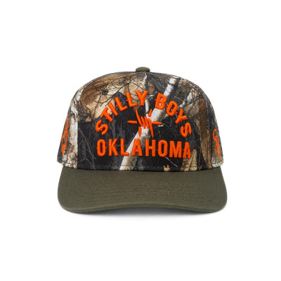 Stilly Boys Clinch snapback hat in hardwoods camo with olive bill and blaze orange embroidered arched lettering, barbed star, and Oklahoma — Stillwater, Oklahoma hunting and wrestling apparel
