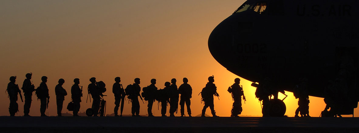 Military personnel loading onto aircraft in front of a sunset