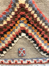 detail 1 Handwoven and hand knotted Ahknif wool rug. Hand spun wool with a natural grey tightly woven ground and a short pile design of diamonds, squares and a patterned border. . Colors of the short knotted pile: chalky red, washed sky blue, dark grey, off-white, washed chalky red brown, red brown, chalky saffron and cream. There is a braided fringe at one end.