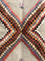 detail 2 Handwoven and hand knotted Ahknif wool rug. Hand spun wool with a natural grey tightly woven ground and a short pile design of diamonds, squares and a patterned border. . Colors of the short knotted pile: chalky red, washed sky blue, dark grey, off-white, washed chalky red brown, red brown, chalky saffron and cream. There is a braided fringe at one end.