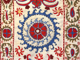 detail. Hand Embroidered Silk Suzani Green Wall Hanging Uzbekistan  Suzani hand stitched wall hanging.  Suzanis are created by the once nomadic people who populated the ancient silk road of Uzbekistan. Suzanis were originally crafted as dowry pieces that a mother would help lovingly create for her daughter’s wedding day. It was believed that the patterns and colors in a suzani held talismanic powers of protection and these powers were magically transferred from the mother into the suzani through the visual impact of her embroidery work. From the studios of Sanjar Nazaroz,  a UNESCO Award of Excellence winner. This size makes a beautiful wall hanging. Shimmering cream colored silk. The embroidery colors: red, periwinkle blue, olive, tobacco, red orange, red brown, sky blue and black and white. 