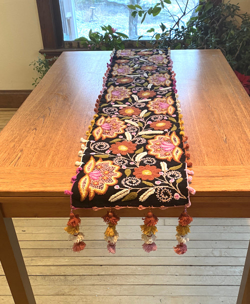Handwoven Hand Embroidered Wool Table Runner A Peru.  The floral patterns are done using different embroidery and crewel stitches. Colors: chalky rust, pale pink, olive, gold, fuchsia, coral and white. The crocheted edge and pompoms on the ends are done with the same colors of the embroidery