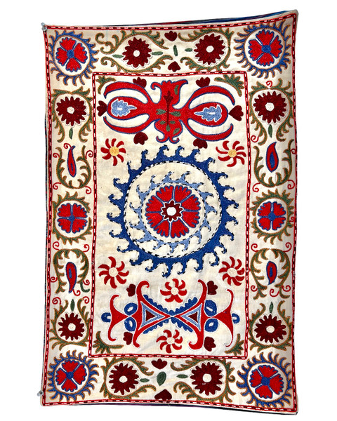 Hand Embroidered Silk Suzani Green Wall Hanging Uzbekistan  Suzani hand stitched wall hanging.  Suzanis are created by the once nomadic people who populated the ancient silk road of Uzbekistan. Suzanis were originally crafted as dowry pieces that a mother would help lovingly create for her daughter’s wedding day. It was believed that the patterns and colors in a suzani held talismanic powers of protection and these powers were magically transferred from the mother into the suzani through the visual impact of her embroidery work. From the studios of Sanjar Nazaroz,  a UNESCO Award of Excellence winner. This size makes a beautiful wall hanging. Shimmering cream colored silk. The embroidery colors: red, periwinkle blue, olive, tobacco, red orange, red brown, sky blue and black and white. 