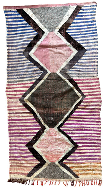 Handwoven rag rug with a dynamic diamond and striped design from weavers in southern Morocco. Beautiful on the floor or on the wall. Colors: shades of periwinkle to royal blue, off- white, violet, charcoal, chalky mauve pink, and more. 3" braided  fringe at one end. Note: this rug has some puckering and doesn't lay completely flat. Size: Approx. 4 feet 11" x 8 feet 11" (57" x 107")
