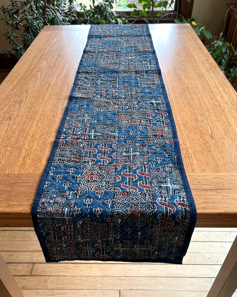 Handmade table runner of block printed fabrics. The fabrics are made with several wooden blocks using the traditional Ajarakh natural dye technique. The fabric is then sewn into a patchwork of various  patterns.  Colors: shades of indigo blue, black, brick red, and creamy white. This is reversible with the back solid block printed pattern in the same colors. There is a solid 1" indigo blue border sewn around. 

