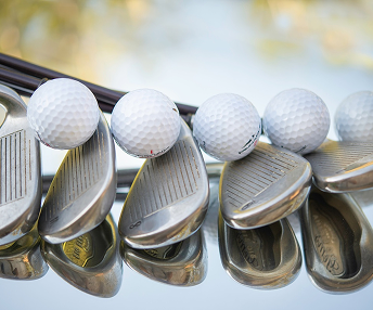 Close-up of golf balls resting on the heads of shiny iron golf clubs.