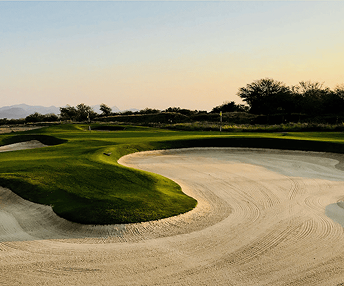 A scenic golf course with manicured green fairways and a sand bunker at sunset.