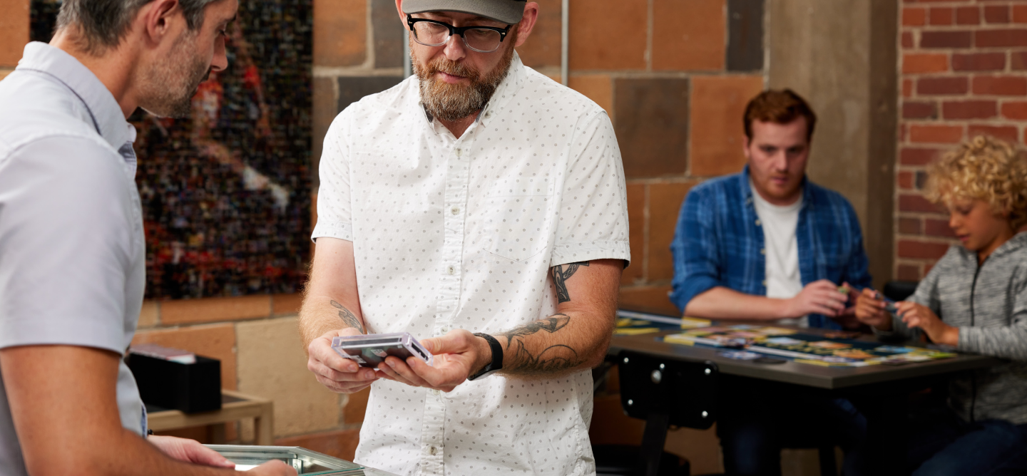 A customer and Midwest Cards store associate view a sports card in a protective case