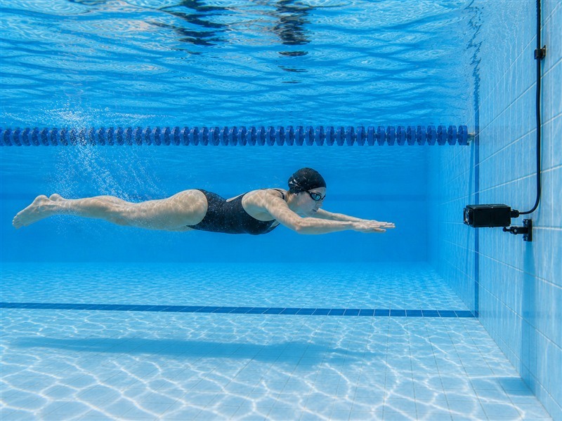 Wall-mounted underwater camera filming an approaching swimmer in a competition pool lane