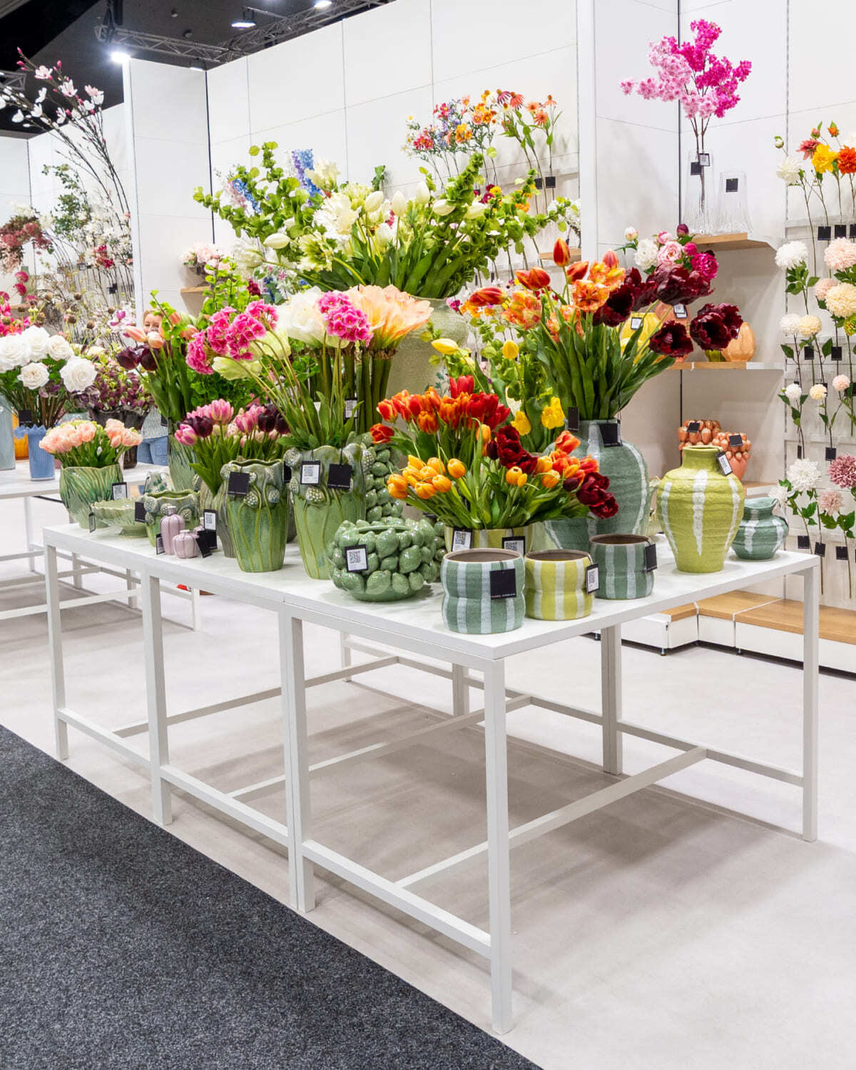 White metal Ditto display tables with white tops, showing vases and artificial flowers