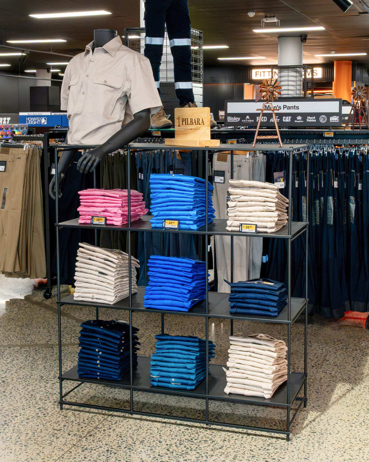 Black Stilt shelving unit with black shelves, displaying folded work shirts in a store