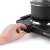 Hand turning dial on black electric single hot plate with pot, close up.