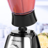 Silver and black blender base with jug above, making pink smoothie, next to pineapple.