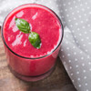 Glass of bright red smoothie with basil leaves, suitable for product listing.