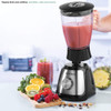 Black and silver blender with glass jug, filled with pink smoothie, beside fresh fruit.