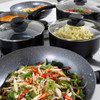 Set of black non-stick pots and pans, some with glass lids, shown in a modern kitchen.