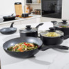 Set of black non-stick pans with cooked dishes, shown on kitchen counter.