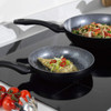 Cookware set displayed with assorted cooked dishes including curry, potatoes, pasta, and salad