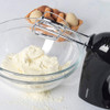 Black electric hand mixer with beaters in glass bowl of cream, eggs in background