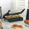 Black panini press with two grilled sandwiches, salad and vegetable skewers nearby