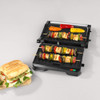 Electric grill with open lid and vegetable skewers, drip tray being removed by hand