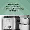 Hand turning dial on stainless steel deep fryer with temperature guide, lemons beside