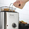 Stainless steel deep fat fryer with basket of cooked chips being lifted by hand