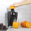 Black electric citrus juicer with glass of orange juice and fresh citrus fruits on kitchen counter