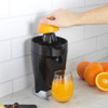 Black electric citrus juicer with glass of orange juice, half lemon, and fresh fruit on kitchen counter