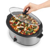 Stainless steel slow cooker with black handles, filled with chopped vegetables and chicken.