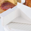 White food slicer in use with cooked meat and cheese platter in background