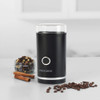 Black electric coffee grinder with glass top, shown with coffee beans and spices on a kitchen counter