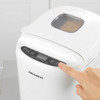Loaf of bread being lifted from white Progress bread maker in kitchen