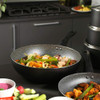 Black non-stick wok with chicken and vegetables, shown on kitchen counter.